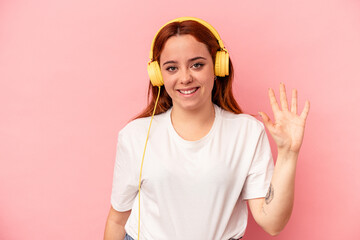 Young caucasian woman listening to music isolated on pink background smiling cheerful showing number five with fingers.