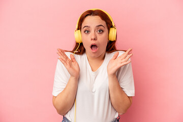 Young caucasian woman listening to music isolated on pink background surprised and shocked.