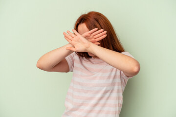 Young caucasian woman isolated on green background keeping two arms crossed, denial concept.