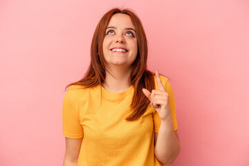 Young caucasian woman isolated on pink background indicates with both fore fingers up showing a...