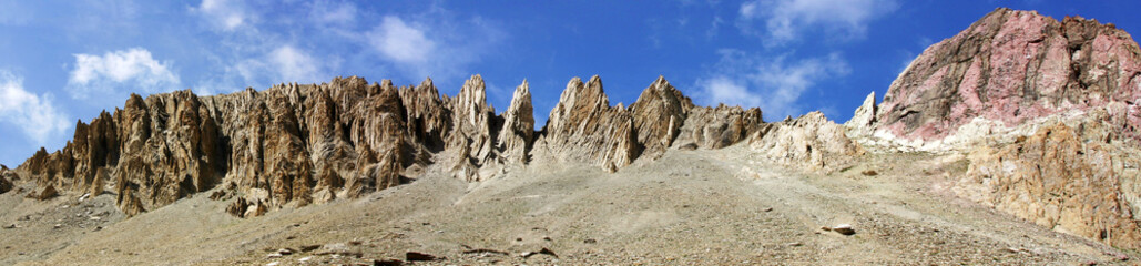 Large panorama minéral en haute montagne, crête rocheuse très découpée et roches roses sur fond de ciel bleu. Alpes françaises, Névache.