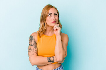 Young caucasian woman isolated on blue background thinking and looking up, being reflective, contemplating, having a fantasy.