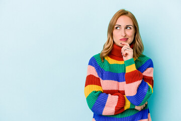 Young caucasian woman isolated on blue background looking sideways with doubtful and skeptical expression.