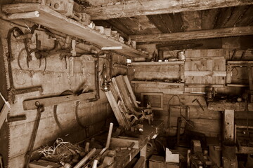 A sepia photo of a medieval workshop including a set of tools for processing wood, metal, farming...