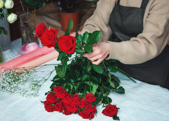 Fototapeta na wymiar Woman florist creating a bouquet of fresh red roses. Cropped image of female florist arranging rose flowers using tools. Concept of working with flowers, floral business. Selective focus