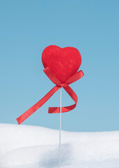 Fototapeta na wymiar Red heart with bows, symbolizing an active, positive, happy person enjoying active time outdoors on snow in nature on sunny winter day. Winter holidays, vacation, christmas, valentine's day concept