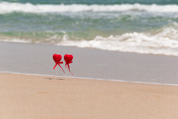 Summer holidays background with two red hearts as symbol of couple in love, sandy beach, sea waves and copy space. Valentine's day, wedding, honeymoon trip together concept.