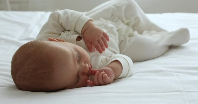 Sweet sleep. Full length view of serene infant child wear white sleeper relax nap on large comfortable bed covered with natural clean linen. Happy little baby dreaming at daytime rest suckle finger