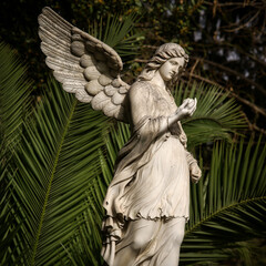 White angel statue with tropical trees on the background in the park
