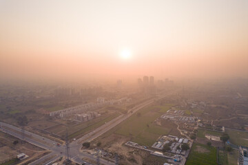 aerial drone shot passing over a building with homes, offices, shopping centers moving towards skyscapers in front of sunset showing the empty outskirts of the city of gurgaon