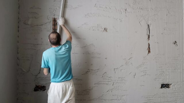 Male Builder Levels Plaster On Wall. Repair in House. Brick Walls. Thick Layer of Plaster has been applied. Alignment. Hard Construction Works. Wall Surface. Overall plan. Recovery. Painstaking Labor