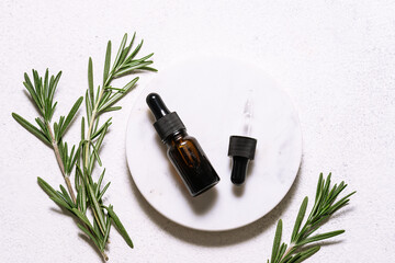 Rosemary essential oil in glass bottle with dropper and fresh green rosemary twigs on white marble...