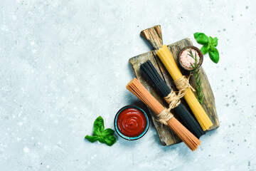 Assortment of dry colorful spaghetti and pasta with cherry tomatoes and ingredients, on a gray...