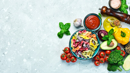 Colored dry pasta in a bowl on a gray stone background. Food. Top view. Free space for text.
