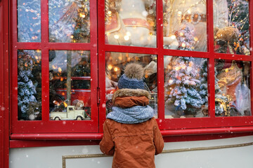 boy watching festive window display at gift store.  New Year and Christmas holidays concept. Child and christmas shop window. winter season