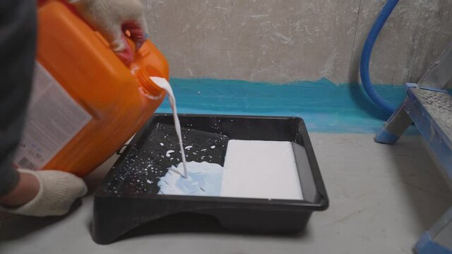 A worker pours primer or paint into a plastic tray. Renovation in the house. A worker pours white soil.