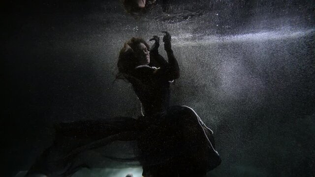 mysterious woman in black gown is floating inside sea, river or pond, underwater enigmatic shot