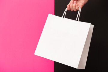 Female hand holding white blank shopping bag isolated on pink and black background. Black friday sale, discount, recycling, shopping and ecology concept.