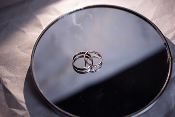 Wedding rings of the newlyweds with white gold lie on the mirror