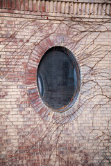 circular window on the side of a brick building surrounded by ivy