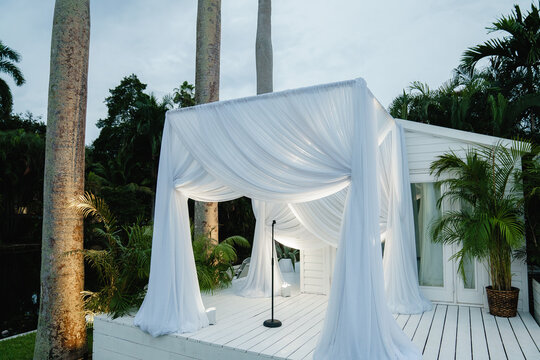 A Stylish White Wooden Arch For A Wedding Ceremony Near The Pool The Square Arch Decorated With An Aerial White Cloth Wedding Arch Setting Outdoor Blue Sky Background 