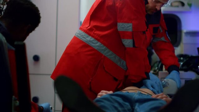 Mixed race paramedics providing heart massage to patient in ambulance car