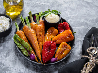 baked roast baby carrots, bell pepper in a plate, basil and spices vegan dish close up, white sauce, goat cheese