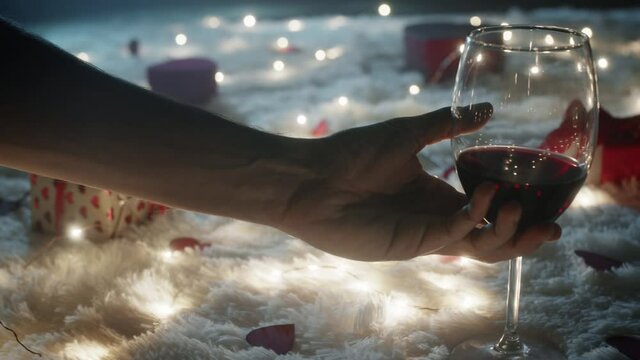 Mano poggia calice di vino e regalo su tappeto bianco per San Valentino