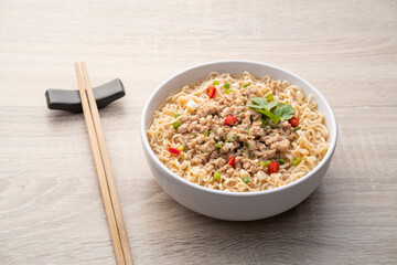 Instant noodle soup with minced pork in white bowl on wood table