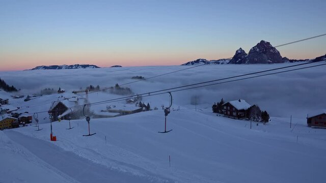Ski lift at tourism resort Stoos at Swiss alps on a sunny morning with colorful sky and sea of fog. Movie shot December 21st, 2021, Stoos, Switzerland.