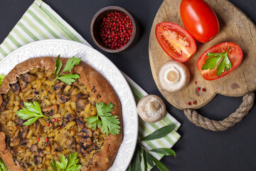 Pie with stewed potatoes and mushrooms on black background