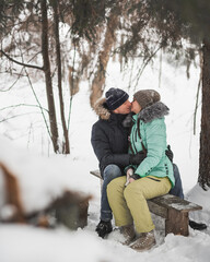 Fototapeta na wymiar Young couple kissing on the bench in winter forest