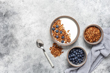 Granola with yogurt and blueberries in a bowl on a gray grunge background. Healthy tasty breakfast. Top view, flat lay