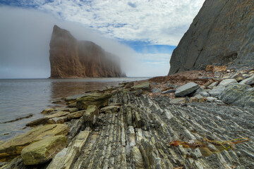 Beautiful shot of fog covering the Perce Rock formations under a blue cloudy sky