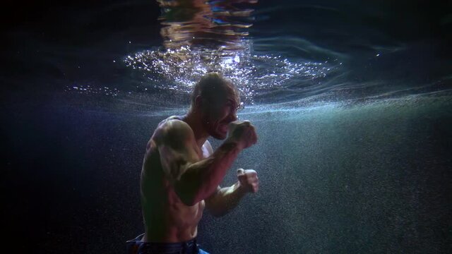 underwater shot of man boxing inside swimming pool, holding breath and fighting