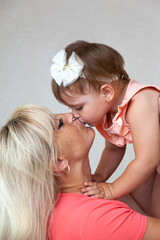 A young mother holds a little daughter in her arms and kisses her on the lips. High quality photo