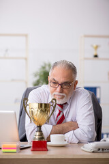 Old male employee being awarded with golden cup