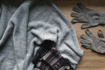Gray sweater, warm gloves and socks on wooden background. Top view.