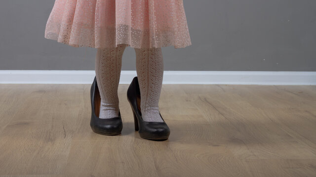 Cute baby girl 2 years old caucasian walks in black mom's big heels in pink prom dress