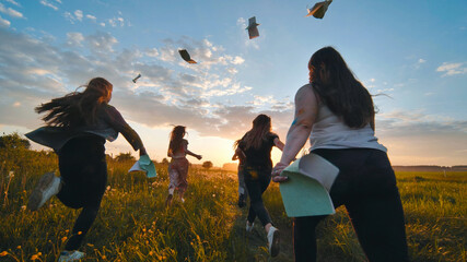 Fototapeta Cheerful students run throwing notebooks after school at sunset. obraz