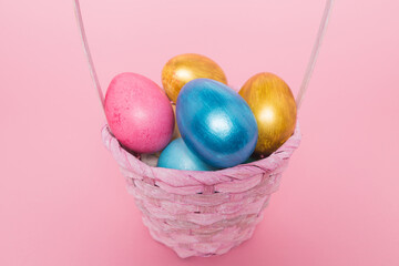 Multi-colored Easter eggs in a basket on a pink isolated background. Easter is a bright holiday.