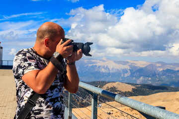 Travel photographer man with professional camera taking photos of  on a top of Tahtali mountain near Kemer, Antalya Province in Turkey