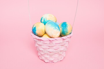 Multi-colored Easter eggs in a basket on a pink isolated background. Easter is a bright holiday.