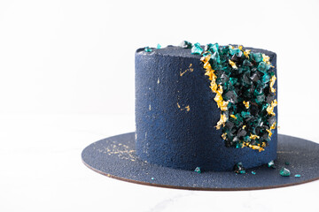 Luxury mousse cake covered with blue velvet coating and decorated with golden petals on the dark...