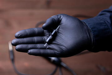 the hands of a permanent makeup artist in black medical gloves on which lies a disposable cartridge for a tattoo machine - obrazy, fototapety, plakaty