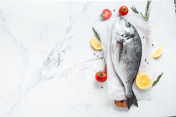 Fresh dorado fish with lemon cut, tomato, razmorin and spices on the white marble background. Flat lay fish ready to cook