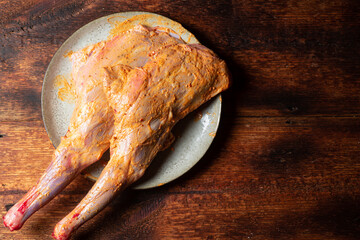Raw lamb leg spread with spices, cooked for cooking on a plate on a wooden background. © Konstiantyn Zap