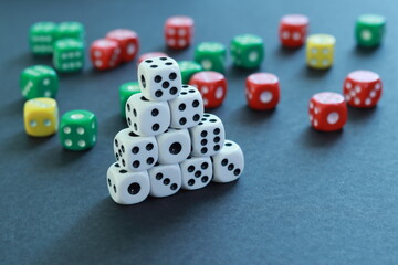 Playing dice mounted in a pyramid and others of several colors in the background on a table