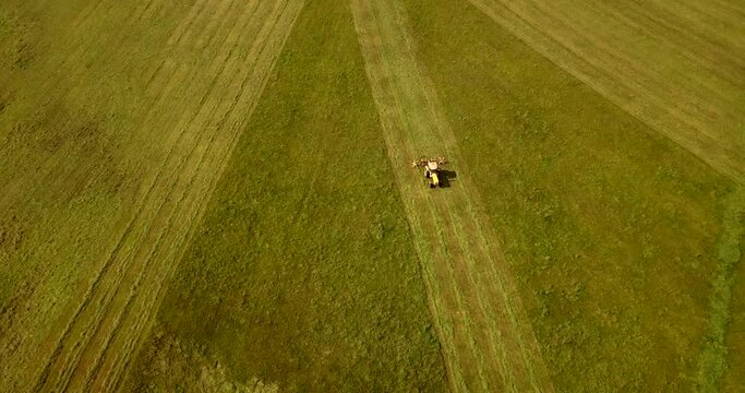 Top down view of the agriculture machinery during haymaking. Flying over the field and tractor, zoom in.