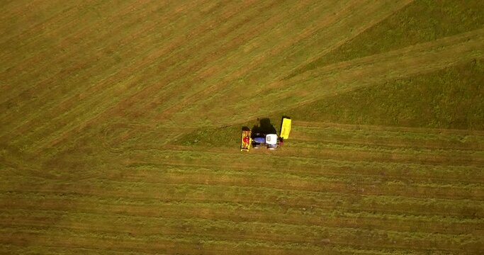 Top down view of the agriculture machinery during haymaking. Flying over the field and tractor.